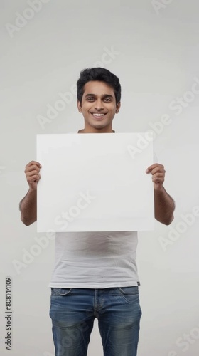 A smiling Indian man holds a white signboard in his hands