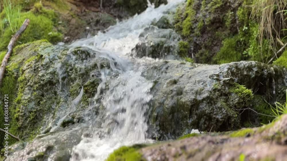Close-up of a small waterfall cascading over moss-covered rocks in a lush, green setting. Close-up of a small waterfall cascading over moss-covered rocks in a lush, green setting.