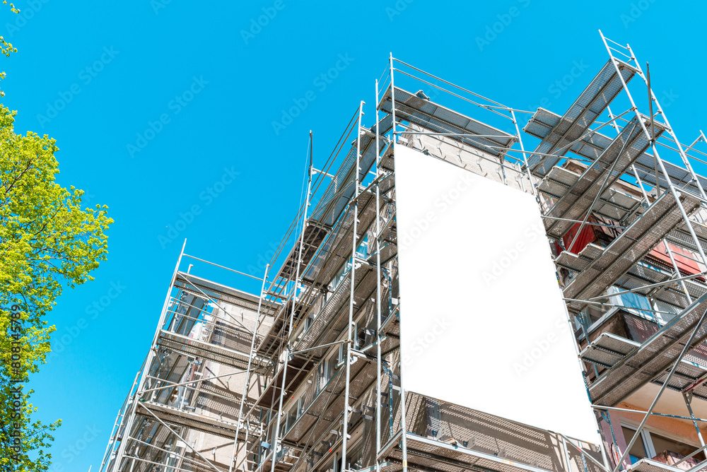 Blank white mockup advertisement hanging on the modern building under construction. Reconstruction of a building with white billboard.