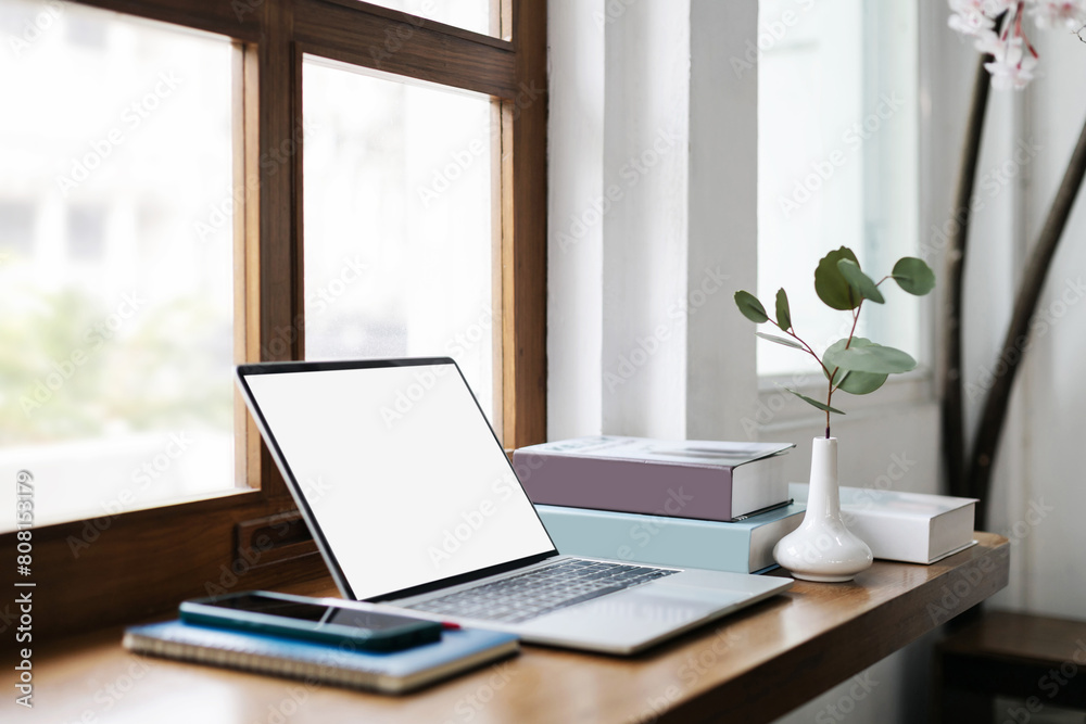 Fototapeta premium Comfortable workplace on wooden counter by the window and laptop, smart phone, note book and pen. vase with small tree inside and a book for read