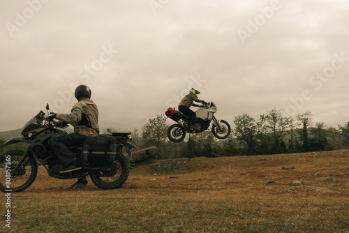 Motorcyclist jumping in moto trip with friend on adventure tourist enduro motorcycle outdoor offroad in mountains