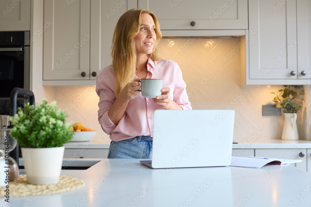 Smiling Woman Working From Home In Kitchen Using Laptop Smiling Woman Working From Home In Kitchen Using Laptop