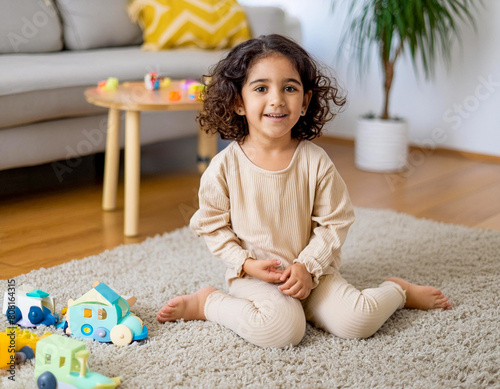 happy 3 year old girl kid playing on house carpet in home living room with children toys photo