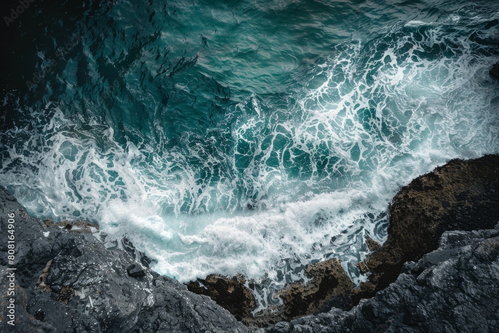 Fototapeta premium A view from a cliff of the ocean meeting the coastline, showcasing intricate patterns and textures of the water and rocks below