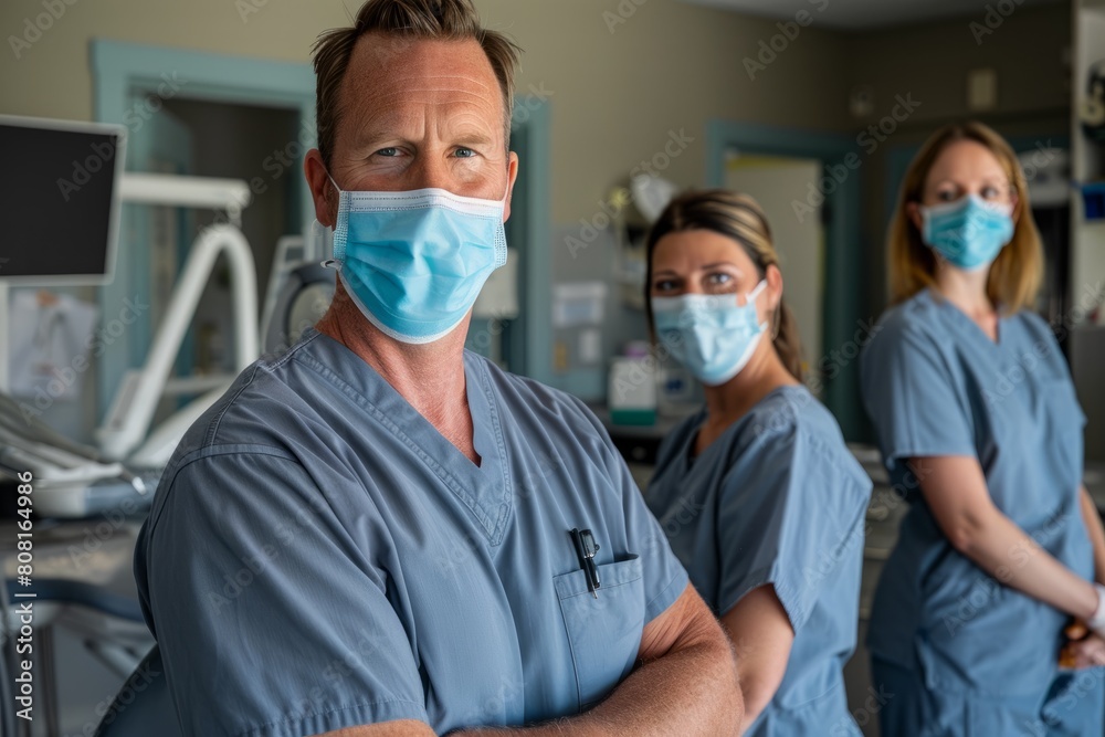 A male doctor and two female doctors, all wearing scrubs and face masks, standing together in a professional setting