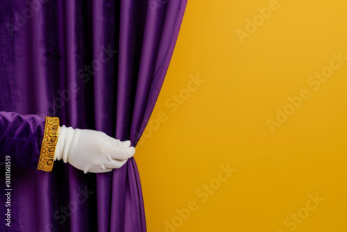 White-gloved hand pulling back a purple curtain against a vibrant yellow backdrop, signifying a grand opening or revealing moment