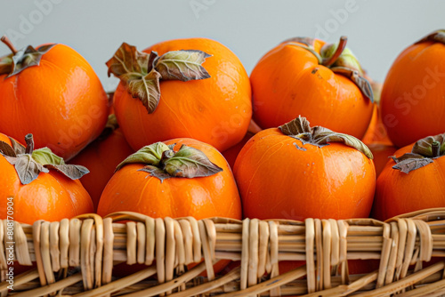 A selection of fresh  ripe Asian persimmons  their orange skins smooth and matte  neatly arranged in a wicker basket against a white canvas.