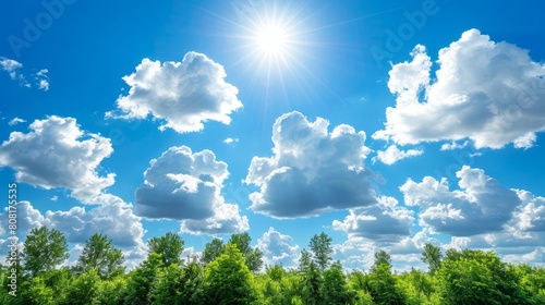   The sun illuminates the clouds in the azure sky, casting light on a line of trees beneath © Mikus