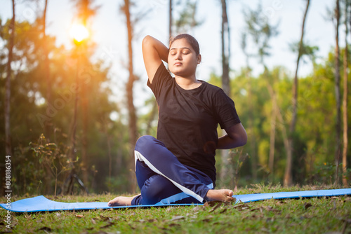 with eyes closed an indian fitness women doing Gomukhasana or Cow Face Pose on a yoga mat at forest during morning