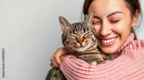   A woman  wearing a pink sweater  smiles closely at a cat as she holds it