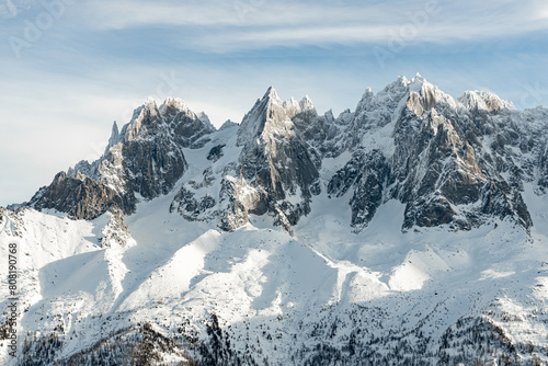 Three snowy mountain peaks in Alps range with blue sky; winter landscape of 3 peaks in French Alps near Mont Blanc and Chamonix with snow and sunshine and trees at the foot of the mountains.