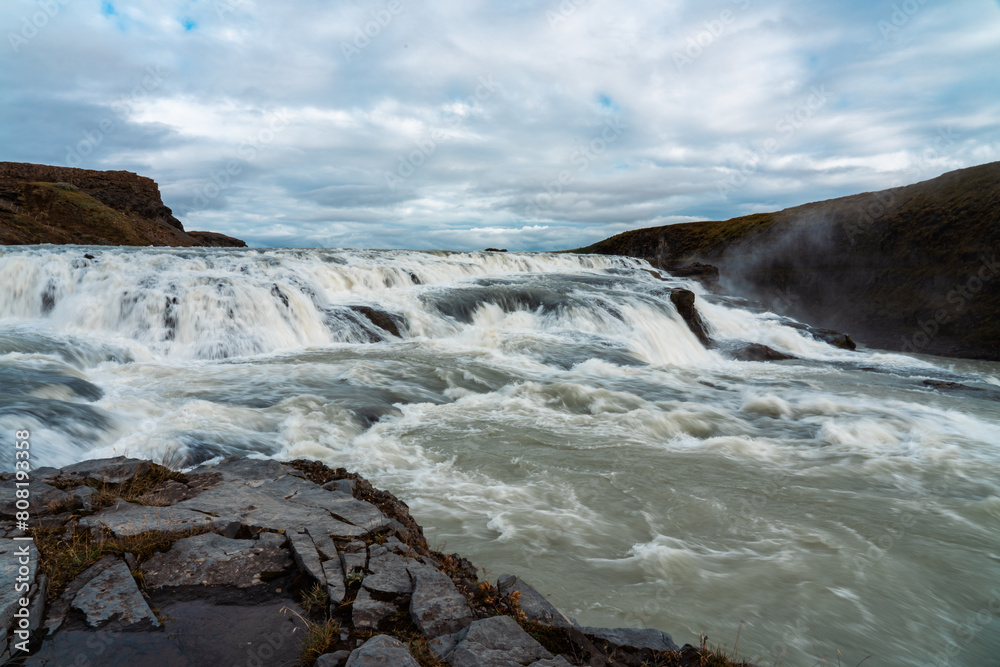Gullfoss waterfalls in Iceland. Cold fog rises from the river bed. Water falls 32 meters. Breathtaking panorama. Queue of tourists in the distance.