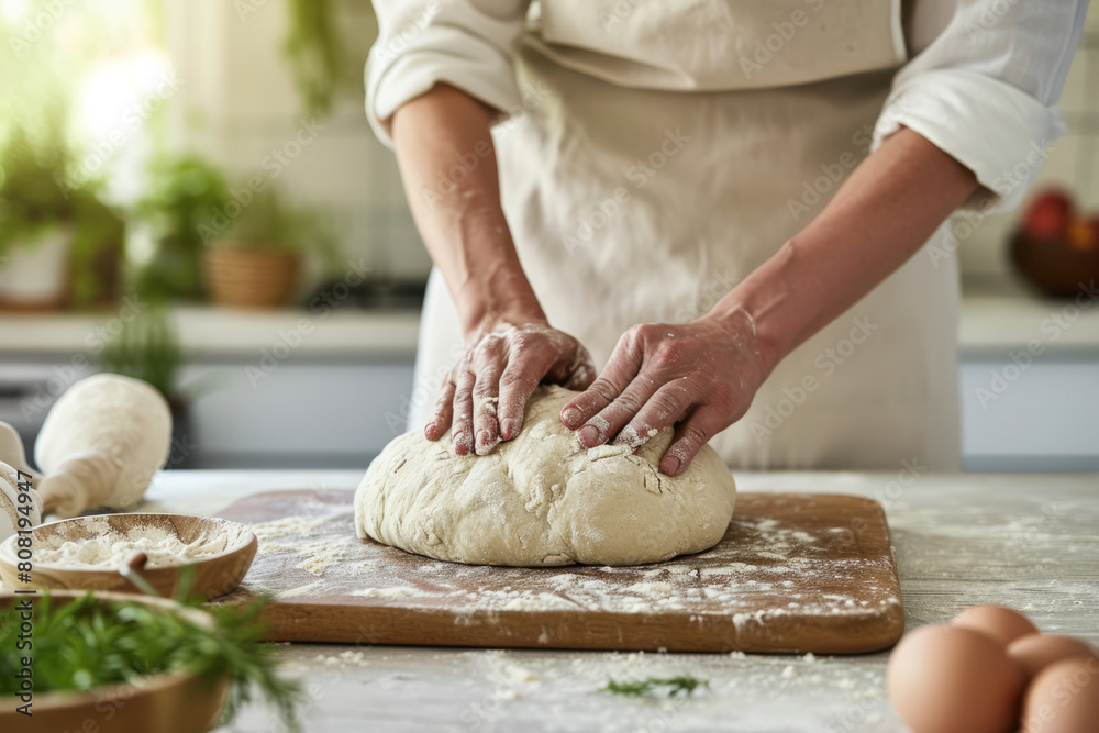 Baker's hands knead dough on the table in a bright kitchen
Baker's hands knead dough on the table in a bright kitchen