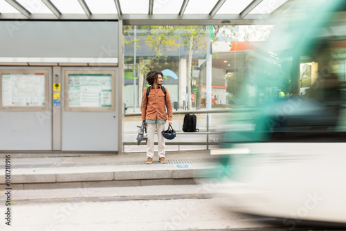 Man waiting at bus stop holding an electric scooter and a helmet photo