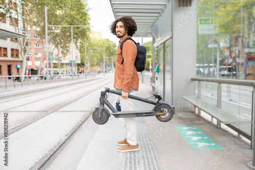 Curly-haired man carrying electric scooter in urban setting photo