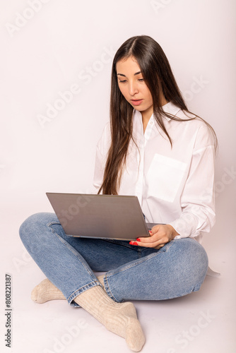 A young woman in white shirt with a laptop sits on white background.Work online