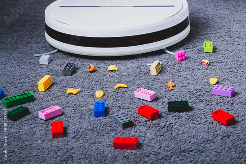 A robot vacuum cleaner cleans children's toys on the floor. Carpet and laminate cleaning. Assembling cubes with a robot vacuum cleaner.