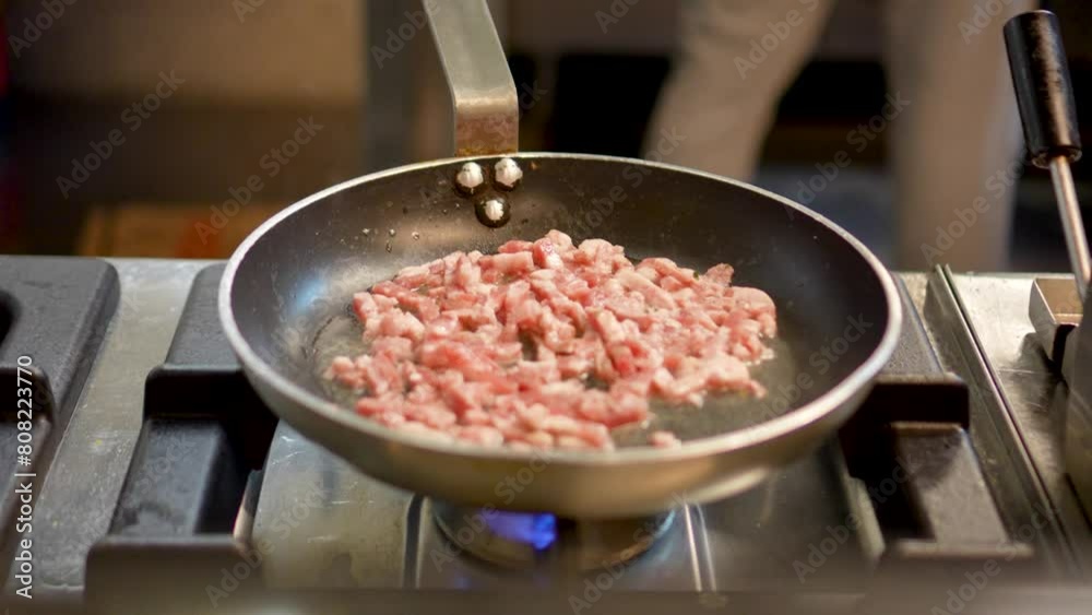 The chef in the restaurant is frying bacon in a large pan
