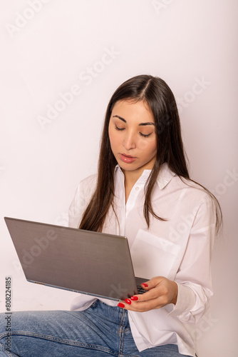A young woman in white shirt with a laptop sits on white background.Work online