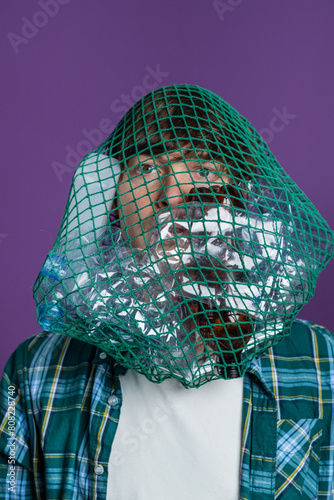 Man's head is ensnared by a green net filled with plastic bottles, symbolizing the suffocating impact of plastic waste on individuals and the environment. 