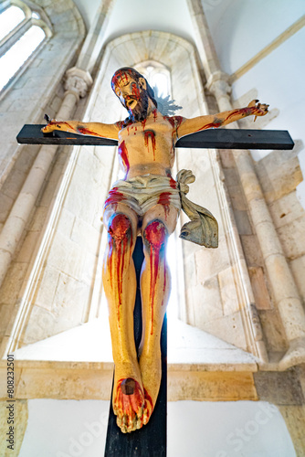 image against sting of the figure of Jesus Christ crucified and bloodied in suffering with blood marks, in the background against light originating from a vaulted window. Santarém-Portugal.