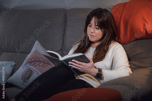 Young adult woman reading a book relaxed on the sofa
