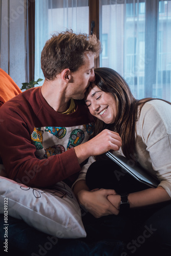 Couple of young adult man and woman in affectionate pose on a sofa. Real life people at home
