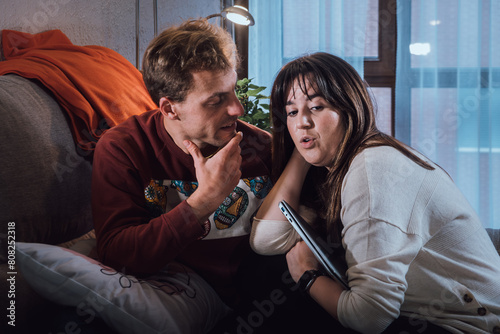 Young adult man and woman couple talking on a sofa in the living room. Real life people at home
