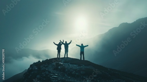 Three people standing at the top of a mountain, arms raised for victory with big mountain and foggy weather behind them photo