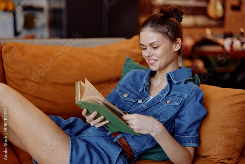 Woman in denim dress reading book on couch in coffee shop interior © SHOTPRIME STUDIO
