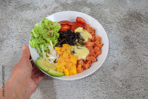 Salmon and mango poke in a white bowl on a woman's hand