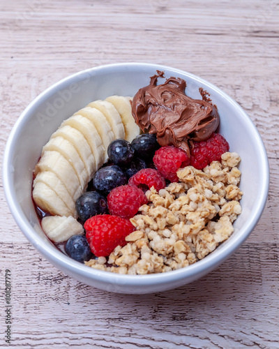 White bowl with red berries, banana, granola and dulce de leche