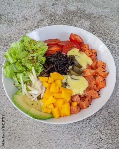 Salmon and mango poke in a white bowl on gray cement background