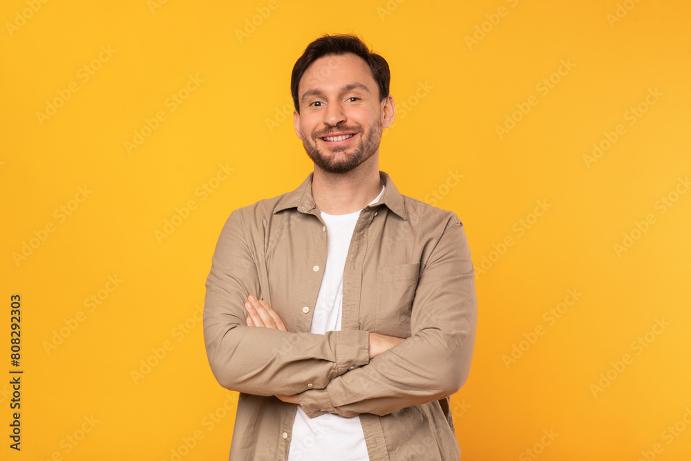 A man is standing confidently with his arms crossed in front of a bright yellow background, displaying a posture of strength and determination A man is standing confidently with his arms crossed in front of a bright yellow background, displaying a posture of strength and determination
