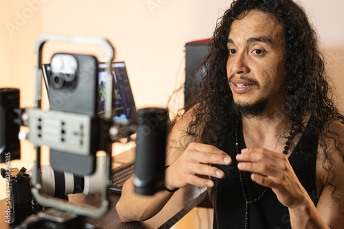 Digital Content Development. A long-haired content creator immersed in his studio, recording videos with his phone mounted on a tripod. Cameras, lights, and a computer are part of his setup.