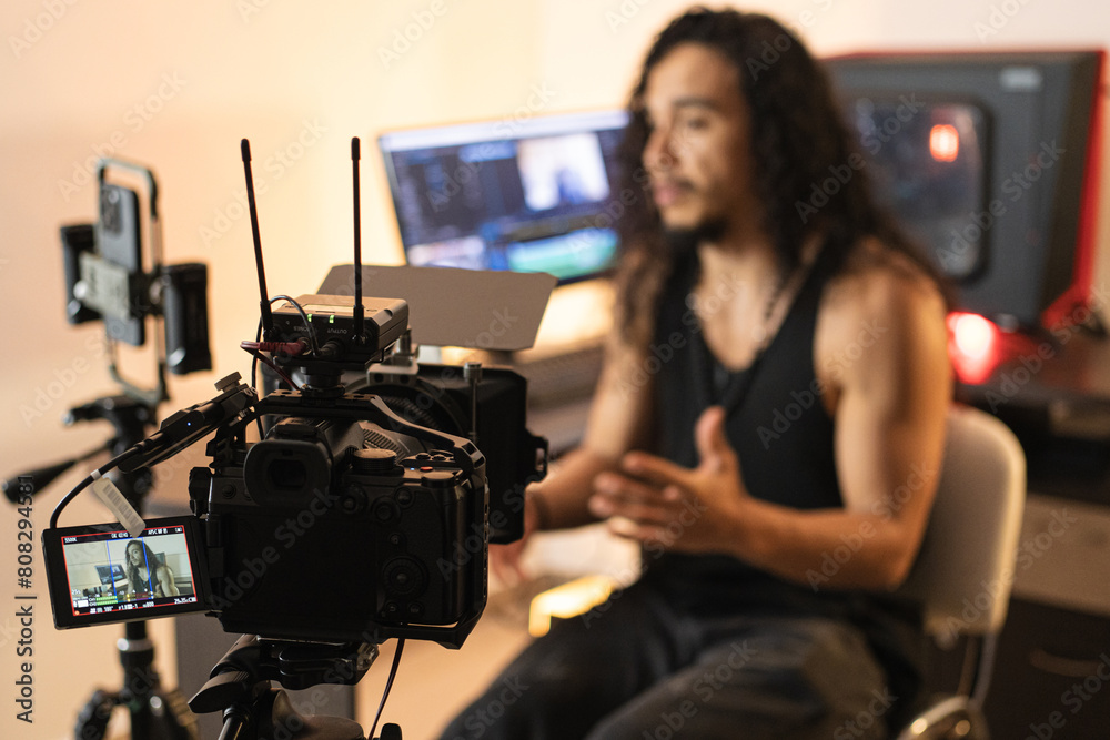 Content Development Workshop. A long-haired content creator immersed in his studio, recording videos with his phone mounted on a tripod. Cameras, lights, and a computer are part of his setup. Content Development Workshop. A long-haired content creator immersed in his studio, recording videos with his phone mounted on a tripod. Cameras, lights, and a computer are part of his setup.