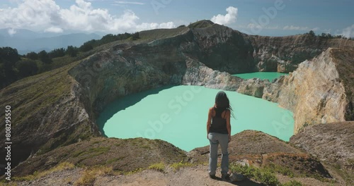 Woman looking on volcano mountain crater edge. Volcanic Kelimutu blue crater lake. Travel destination. Beautiful wild landscape. Female tourist on summer vacation. Lifestyle holiday concept. Back view photo