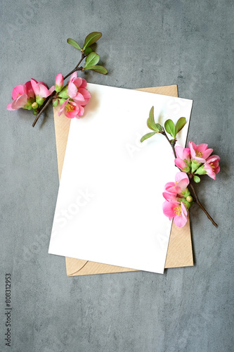 Blank white greeting card with brown envelop and flowers on grey background.