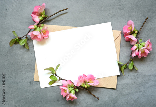 Blank white greeting card with brown envelop and flowers on grey background.
