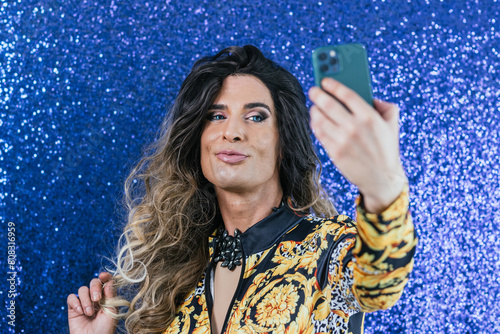 Confident drag queen taking selfies with a mobile phone over a glitter background. photo