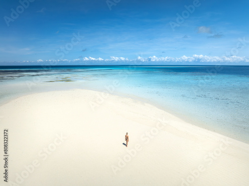 Aerial view of alone young woman on the sandbank in ocean, white sand, blue sea during low tide at sunny summer day in Nakupenda, Zanzibar island. Top view of girl, sand spit, water, sky with clouds