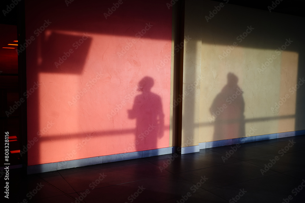 Fototapeta premium The shadow of a man on the wall, a man watching the departure screen. Silhouettes of people with a reflection on the wall .The shadow of a man on a concrete wall, red in hue. High quality photo