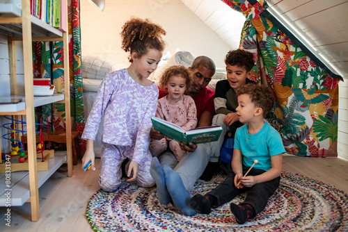 Father reading a book with his children in a colorful attic room photo