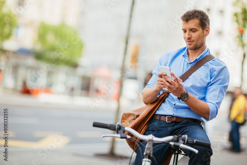 Smiling businessman using smartphone while leaning on bicycle in urban setting