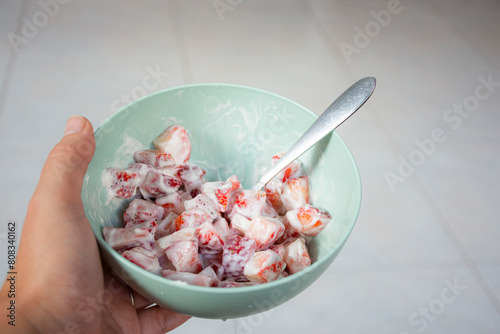 A person holding a turquoise bowl with strawberries cut into small pieces mixed with cream and a spoon