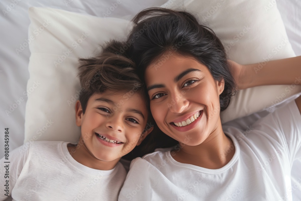 Heartwarming top view of a smiling mother and her young child lying in bed, sharing a close and affectionate moment, with their heads touching, emanating joy and familial love Heartwarming top view of a smiling mother and her young child lying in bed, sharing a close and affectionate moment, with their heads touching, emanating joy and familial love