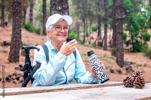 Portrait of happy senior active woman in a trekking day in the woods drinking from water bottle. Old people and healthy lifestyle concept