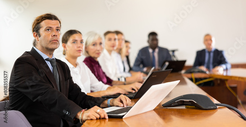 Confident man with laptop sitting and listening speaker at business meeting