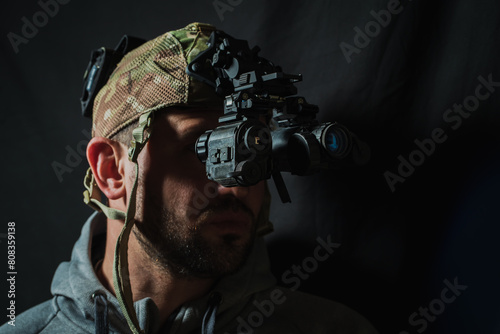 Portrait of a military contractor with a beard with a binocular night vision device on his head.