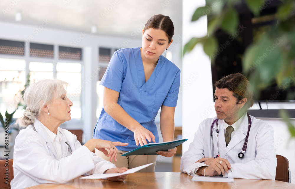 Fototapeta premium three doctors are sitting at table animatedly and actively discussing work